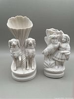 Front view of two Parian ware spill vases: one with two dogs beside a cornucopia and one with a girl and goat figure.