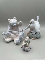 Three Royal Copenhagen porcelain figurines showing polar bears playing, doves on a rock, and a mermaid with a fish.
