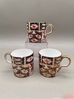 Three Royal Crown Derby Imari demitasse cups shown stacked and side by side, displaying blue, gold, and floral design.