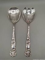 Photo of two silver plated salad servers showing the full length and floral detailed handles.