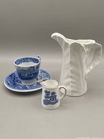 Copeland Spode Italian demitasse cup and saucer in blue and white, Royal Worcester fern leaf designed small creamer, and Coalport Willow miniature creamer arranged on gray background.