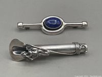 Two sterling silver brooches: one with an oval lapis lazuli cabochon and Danish modern style; the other an Art Nouveau flower holder pin featuring an angel figure.