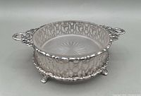 Angled side view of sterling silver butter or condiment dish showing openwork pattern, two handles, and glass liner inside