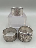 Three sterling silver napkin rings displayed on a white block with monograms and engravings visible