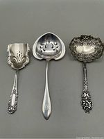 Three sterling silver serving scoops arranged side by side, showing size, shape and pierced designs on each scoop along with their ornate handles.