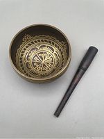Top-down view of brass Tibetan singing bowl showing interior gold-toned intricate patterns next to dark wooden mallet