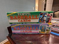Two sealed Topps complete baseball card boxes stacked on a table, showing 1990 and 1989 official sets with prominent player images on boxes.