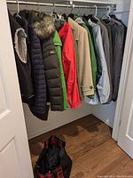 Photo showing multiple winter coats and a vest hanging on a clothing rod, various colors and brands visible