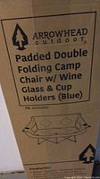 Box front label showing Arrowhead Outdoor brand and features including padded double folding design, wine glass and cup holders, color blue.