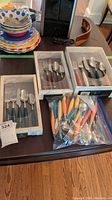 Overview of Fiesta flatware boxed sets and loose flatware in plastic bag, various handle colors displayed on kitchen table.