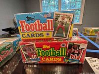 Two unopened Topps Football Cards box sets from 1989 and 1990 on a table near a window.