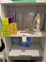 Shelf with Rowenta iron, cartons of parchment paper, Reynolds plastic wrap, plastic organizers, and Lysol spray below.