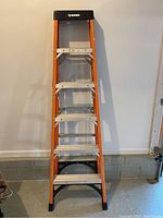 Full view of the 6-foot orange Husky stepladder standing upright against a wall in a garage.