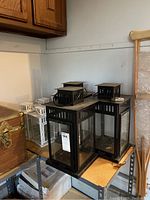 View showing 4 white metal lanterns and 3 black metal lanterns on shelving in garage with visible dust, dirt, and smudges.