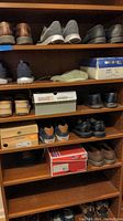 Multiple pairs of men's size 12 shoes on wooden shelves including dress, casual, and tennis shoes.
