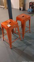 Pair of orange metal stools viewed from an angle, placed on concrete floor in basement.