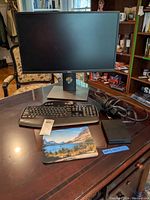 Dell monitor, wireless Logitech keyboard, black docking station, and mouse pad arranged on a polished wooden desk.