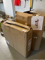 Two cardboard boxes on garage floor, one large and one medium sized, with the larger box showing a snowman measuring stick taped on the front