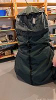 Large black fabric tree storage cover in basement surroundings, folded and standing upright.