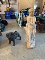 Image showing the classical woman sculpture and the dog sculpture together in a garage setting, highlighting their size and form.