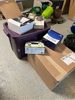 Overall shot showing all included items in the lot: Rubbermaid tub, boxed solar spot lights, power cord, and other items