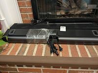 Two Sonos Playbar soundbars stacked on a brick hearth with plastic wrap on one unit and two power cables visible