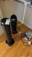 Photo shows two black ceramic tower space heaters and one silver Utopia space heater on hardwood floor.