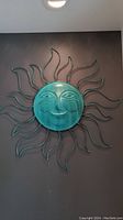 Full view of turquoise metal sun wall art with a face and solar rays, mounted on wall.