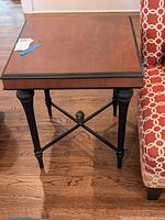 Full view of the wood side table showing square top with scratches and black legs with crossbars.