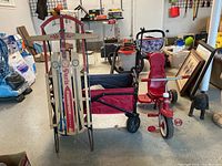 Photo showing red Radio Flyer tricycle with parent push handle, folding wagon in red and black, and Paris Champion wooden sled with metal runners