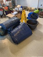 Photo showing folded black plastic tarps, plastic tubs, caution wet floor sign and black woven-pattern planter