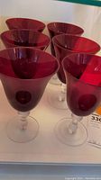 Six deep ruby red glass stemware glasses with clear segmented stems, arranged close together.