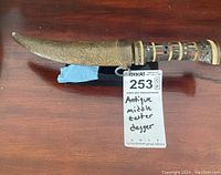 Full view of antique Middle Eastern curved cutter dagger showing handle and ornate sheath on a wooden surface