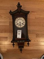 Front view of vintage wooden wall clock with Roman numeral dial and glass front panel.