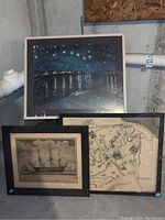 Three framed artworks displayed leaning against basement wall