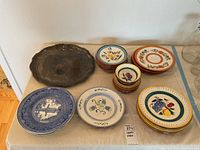 Wide view of all plate sets and metal platter on table showing distinct hand painted fruit plates and Princeton College plates