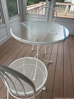 Photo showing white metal framed round glass top table and one white metal chair in an enclosed porch area