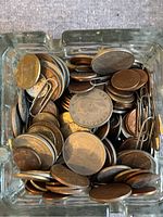 Close-up of assorted coins in a glass ashtray showing various denominations and metal types.