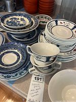 Stack of blue and white salad plates and bowls with blue willow pattern, including teacups with floral and blue zigzag patterns and matching saucers.