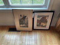 Two framed prints leaning against window sill on hardwood floor, one black-and-white and one color