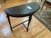 Full view of the small half-round wooden table showing the tabletop shape and wood finish.