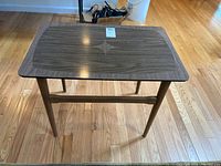 Front view of the small rectangular mid-century modern table showing the wood grain top with star-shaped lighter wood inlay and four tapered legs on hardwood floor.