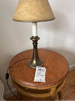 Small round wooden top table with a small brass-base lamp placed on it, with tag showing lot number.