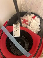 Photo showing red and black spin mop bucket with mop handle inside and two microfiber mop head refills in plastic bag in bucket