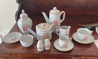 Overall arrangement showing most service pieces on a wood surface: teapot, coffee pot, sugar bowl, creamer, tea caddy, canister, cups and saucers, salt & pepper shakers