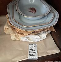 Photo showing four Spode Copeland Trade Winds dishes including plates and platters stacked, with visible gold trim and red ship design.