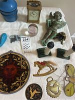 Photo showing most lot items arranged on white cloth including brass clock, cherub figure, lighthouse bookends, sun catchers, and brass rocking horse