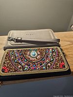 Photo showing close-up of the tan leather wallet with wristlet and the multi-coloured beaded wallet lying side by side on a wooden surface.