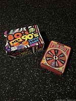 Photo showing the 80's/90's Trivia Game box with colorful retro design next to The Ultimate Pub Quiz card set with vintage graphic design showing multiple quiz categories.