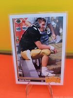 Photo of the 1991 Upper Deck Brett Favre rookie card showing him in football uniform sitting during game or practice.
